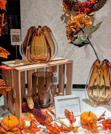 Herbstdekoration mit Kürbis, Laub und Herbstkranz in einem Schaufenster mit Glasvasen in Farbe bernstein/braun und Windlicht aus Glas in Farbe taupe