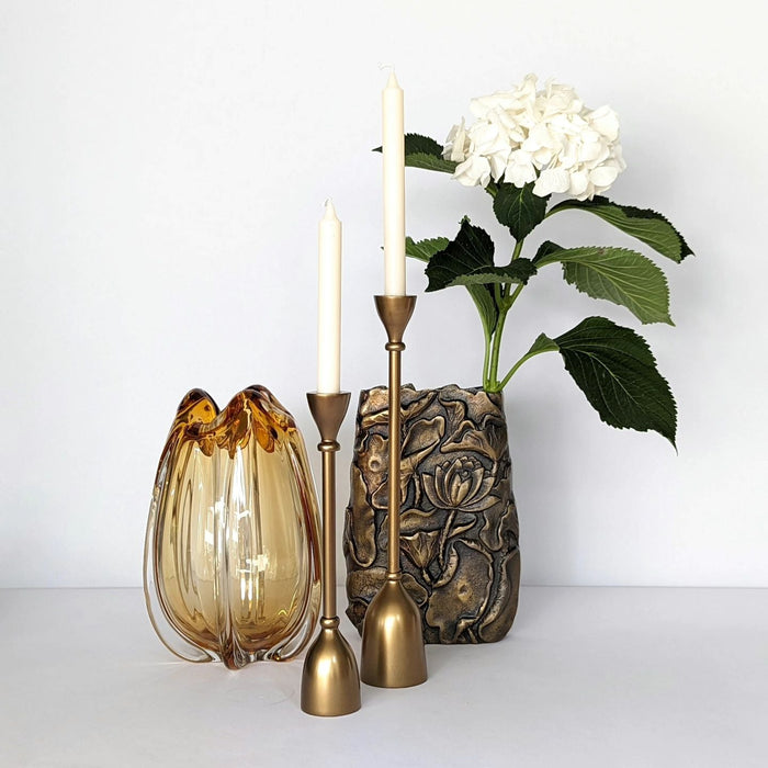 Moodbild mit 4 Produkten: 2 goldene Kerzenständer, 1 goldene Aluminiumvase, 1 bernsteinfarbene Tulpenblütenvase